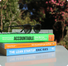 A stack of books with a pair of sunglasses on top: "Accountable" "Let my people go surfing" and "the lean startup" are the book titles.