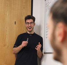 Tumelo team member Harry stands giving an enthusiastic presentation during a whiteboard session.